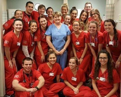 Marsha Hughes-Gay poses for a photo with a group of IU School of Nursing students who are wearing their red scrubs