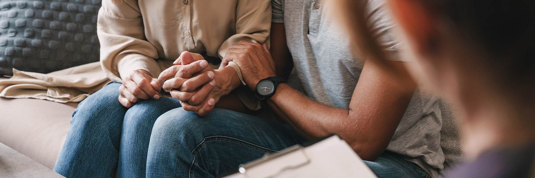 Two people sitting with hands clasped near an individual with a clipboard
